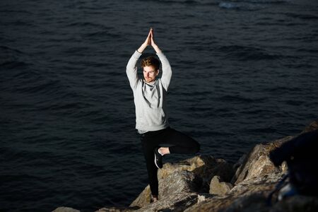 Young redhead practicing yoga, Vriksasana tree posture, to concentrate and help him with his...