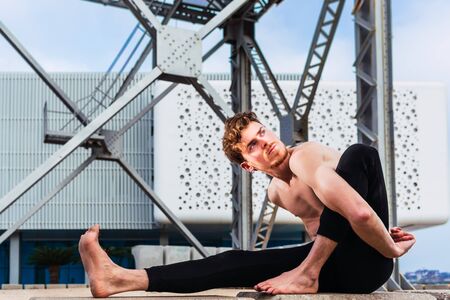 Young man  in the city in the yoga position ardha matsyendrasana stretching and relaxing her body...