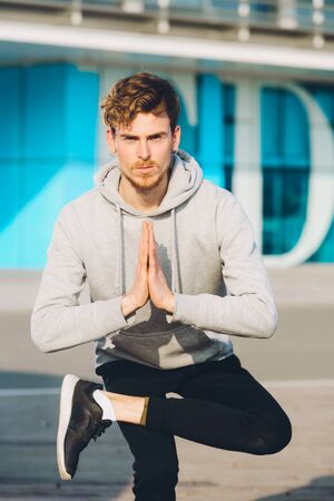 Young redhead man sportsman performing the Namaste Yoga greeting while practicing on a city street.の写真素材