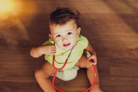 Complaining baby sitting on the floor while playing with a toy stethoscope.の写真素材
