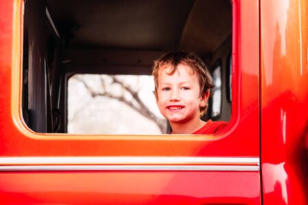 Portrait of a boy with a really dirty face, smiling from inside a red car.