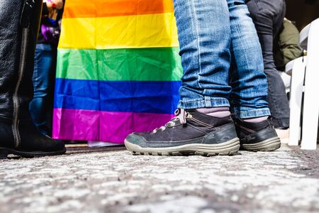 Group of people walk alongside a flag of the LGBT collective claiming equal rights during a protest march in the streets of a large city.の写真素材
