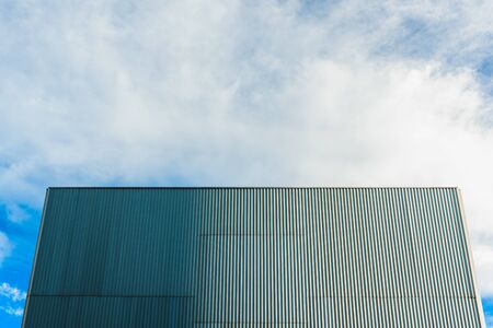 Aluminum wall at the back of a smooth windowless building and blue sky.