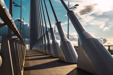 Sunset dramatically over the steel cables of a sidewalk on an urban bridge in Valencia.