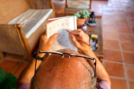 Retired man spends his time solving boring crosswords on the porch of his house.の写真素材