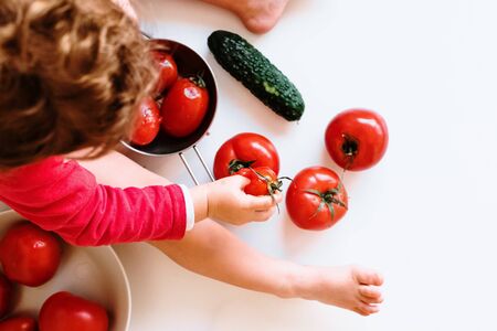 Detail of some ripe red tomatoes between the legs of a girl who plays with them, white background.の写真素材