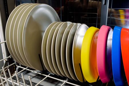 Clean ceramic dishes and colorful plastic in the tray of a washing machine.