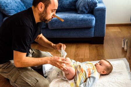 Dad cleaning his baby's dirty ass, changing the stinky diaper with a nose clip, fatherhood and humor.の写真素材