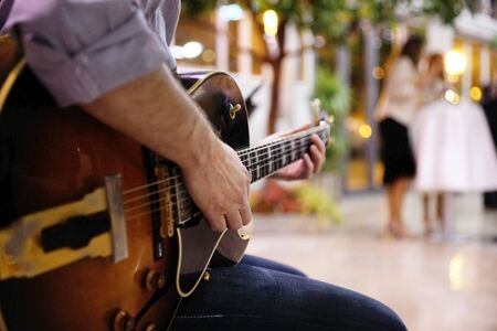 Detail of the hand of a young man playing an electro-acoustic rock guitar outdoors.