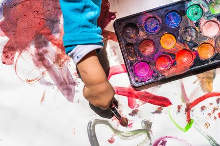 A girl paints watercolors with her stained hand and everything is a mess.の写真素材