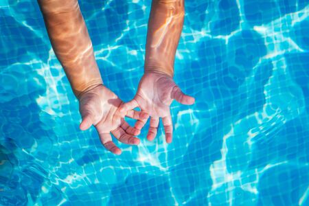 Baby hands in the water of a pool with palms up in the sun.の写真素材