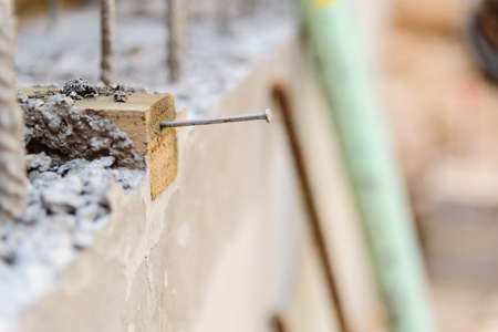 A steel nail nailed to a wooden block on a construction site, with the background out of focus.