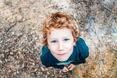 Blond boy making funny gestures and faces photographed from above with natural ground background.の写真素材
