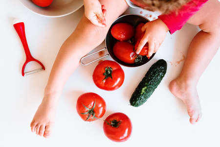 A barefoot baby plays at biting red tomatoes and smearing its juice.