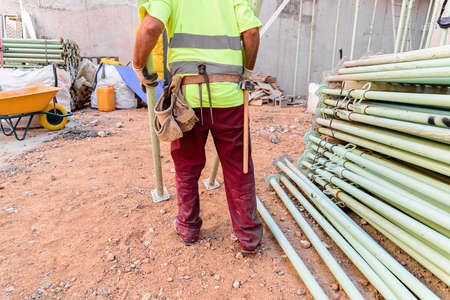 Unrecognizable construction worker working on a construction site with a yellow safety bib.