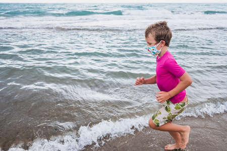 A boy runs along the shore of the beach wearing a face mask during the new normality.の写真素材