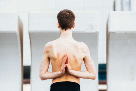 Yoga posture inverted prayer or Namaste hands on the back performed by a young man outdoors.の写真素材
