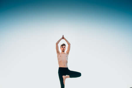 Young man in a Namaste greeting position while freeing his mind from worries in tree pose.の写真素材