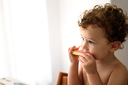 Little girl eats vegetables sitting in the dining room, with blank negative space.