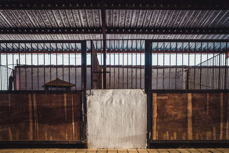 Old box for animals in an empty stable with bars and wooden doors for horses.