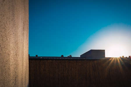 Summer is ending, the intense sun hides behind the roofs of a building.