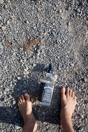 Valencia, Spain - August 23, 2020: An empty bottle of Jack Daniels whiskey lying on the ground next to a drunk man lying on the ground.のeditorial素材