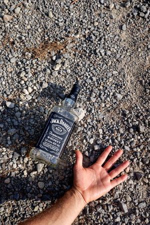 Valencia, Spain - August 23, 2020: An empty bottle of Jack Daniels whiskey lying on the ground next to a drunk man lying on the ground.のeditorial素材