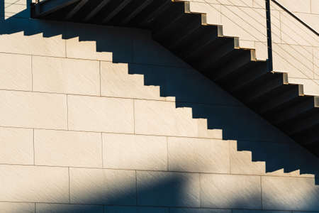Minimalist wall with shadows from the upper steps of a modern stone staircase.の写真素材
