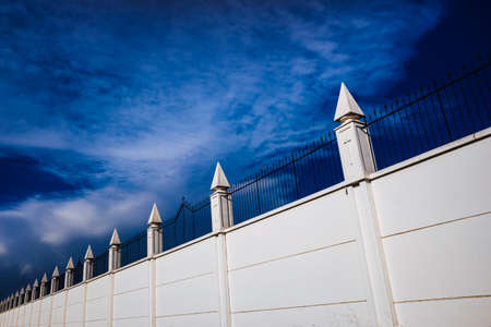 Metal grating of a cemetery with a cross on a white wall, copy space and deep and vibrant blue sky background.の写真素材