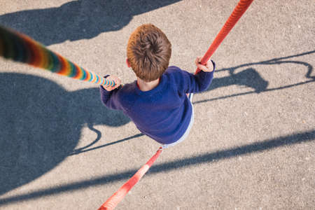 Young boy clinging to a rope in an adventure playground.の写真素材