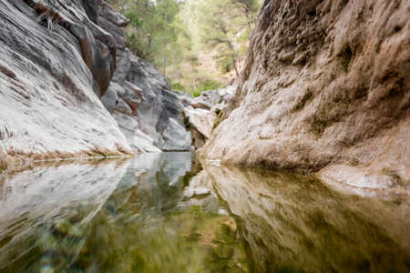Calm watercourse that flows in the rocky bed reflecting the forest in its waters.の写真素材