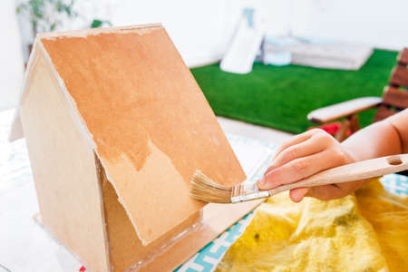 Detail of the hand of a child with a brush painting a wooden board as a craft at home.