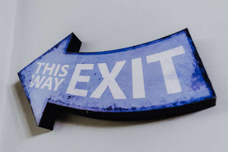This Way Exit written on a decorative blue wooden arrow hanging on a wall.