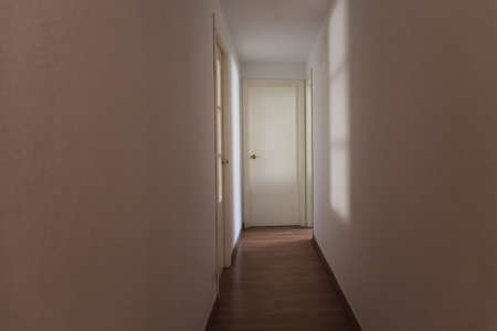 Scary light-walled hallway with a closed door illuminated by the dim shadow of a window, copy space.