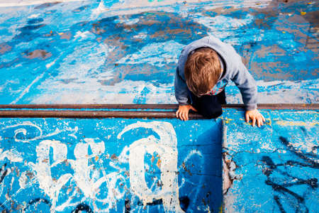 Child loitering inside an abandoned skating area, painted blue, and imagining able to skate.の写真素材