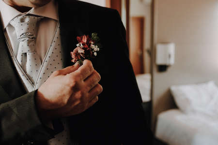 A groom places a floral pin on the lapel of his jacket, film grain added.