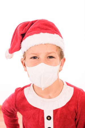 A child like Santa Claus, isolated on white background, wears a mask on his face to protect himself from viruses at Christmas.の写真素材
