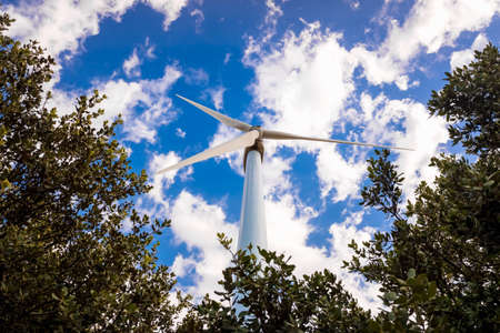 Tall, modern wind turbines spinning to generate renewable electricity with a cloud sky in the...