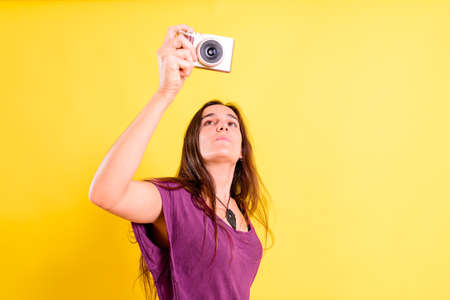 Pretty young girl takes photos with an evil camera, isolated on yellow studio background.