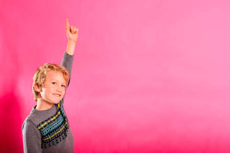 Boy points his finger up with his hand up while laughing, isolating on pink background.の写真素材