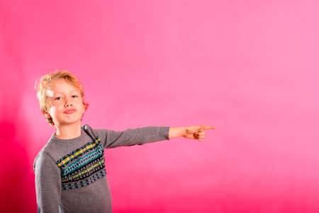 Funny little boy points his finger forward while laughing, isolating on pink background.の写真素材