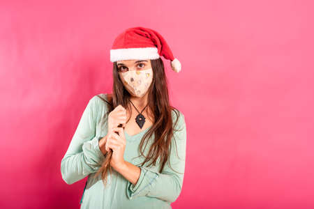 Pretty young girl in Santa hat and mask isolated on pink background during pandemic.の写真素材