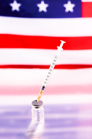 Medical vials with the covid vaccine with a syringe, in front of an unfocused American flag.の写真素材