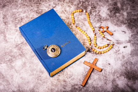 Bible, rosary and Christian crucifix next to a pocket watch, viewed from above.の写真素材