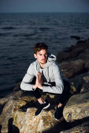 Young man by the sea at dusk practices yoga with the sound of the waves to relax.