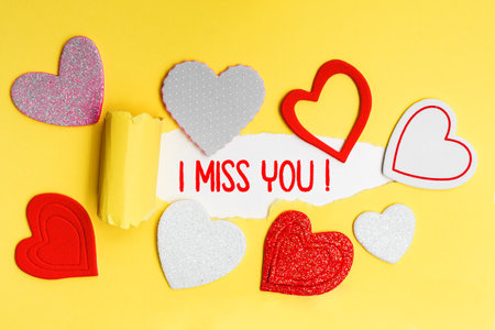 English text I Miss You written in red letters on a yellow card with love hearts.