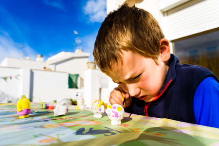 Child uses his free time as a hobby painting plaster pieces outdoors.