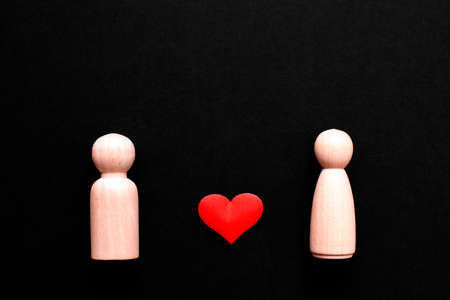 Wooden figures representing a couple of man and woman in love, with a beautiful red heart, isolated on a black background.の写真素材