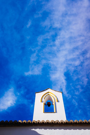 Bell tower of a church with white walls, against the background of a beautiful blue sky.