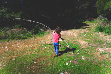 A little girl, with her back turned, has fun playing with sticks and branches in a forest.の写真素材
